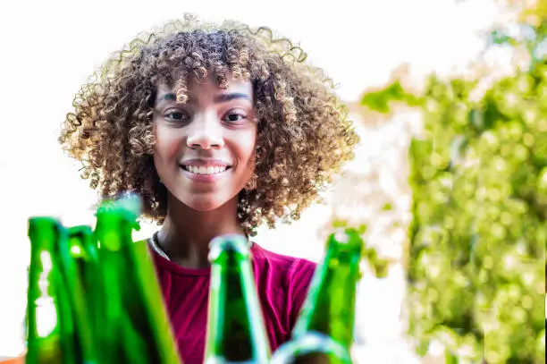 a young black woman putting bottles to recycle in a recycling holder