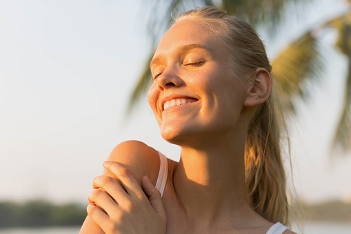 A blonde woman smiling outdoor in nature enjoying the warn sunlight on her pretty face.