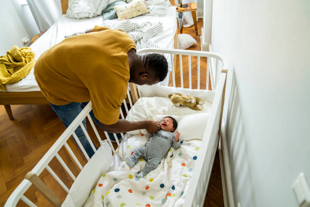 istock Father playing with crying son lying in crib 1254725547