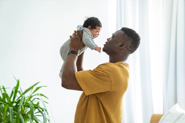 Playful father lifting newborn baby Mid adult man playing with baby boy. Playful father is lifting newborn son. They are in bedroom at home. father and baby stock pictures, royalty-free photos & images
