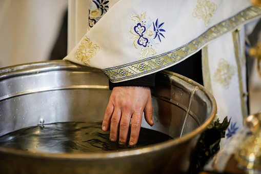 Details with the hand of an Orthodox priest testing the warmth of the water in the baptismal font.