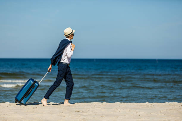 istock Young elegant man walking with suitcase at seaside 1254731378
