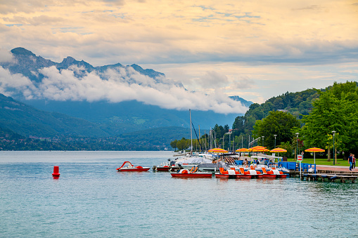 A view of the Lake at Annecy, France, with the setting sun turning the low cloud orange on the horizon and the Alps visible through the cloud.