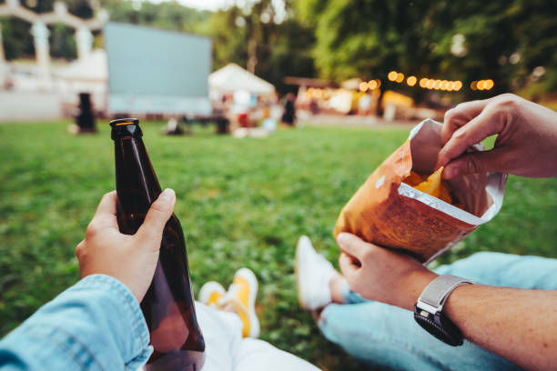 woman hand holding beer bottle man hand holding chips open air cinema woman hand holding beer bottle man hand holding chips open air cinema copy space woman legs open stock pictures, royalty-free photos & images