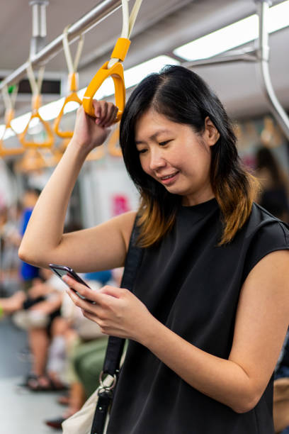 Asian female Millennial using smart mobile phone inside MRT Asian female Millennial using smart mobile phone inside a city train, MRT. singapore mrt stock pictures, royalty-free photos & images