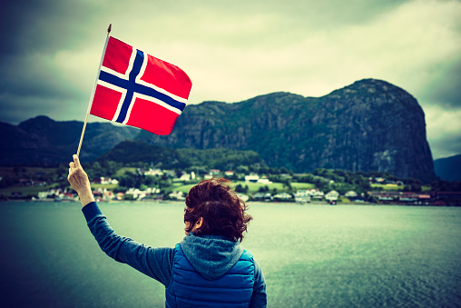 Female tourist with norwegian flag enjoying fjord Lysefjord view. National route Ryfylke. Vacation and travel.