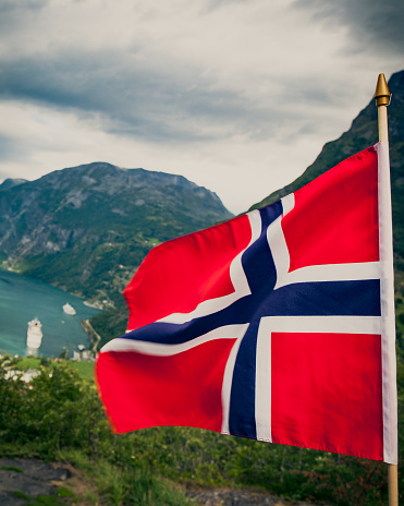 Norwegian flag and beautiful view over Geirangerfjorden from Flydalsjuvet viewing point. Tourist attraction. Tourism vacation and travel.