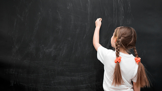 little girl writing with chalk on chalkboard in school