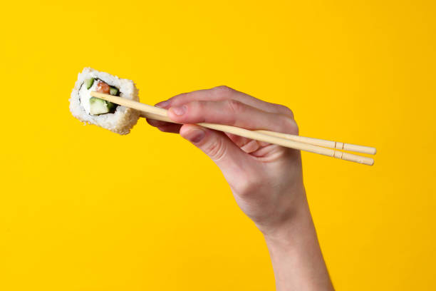 istock Hand holds sushi roll with chopsticks on a yellow background. Japanese kitchen 1254749351
