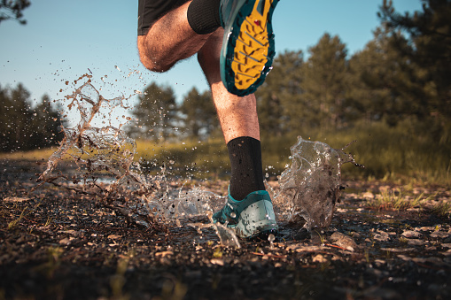 Shot of the legs of a man who is stepping into a puddle while running through the forest.