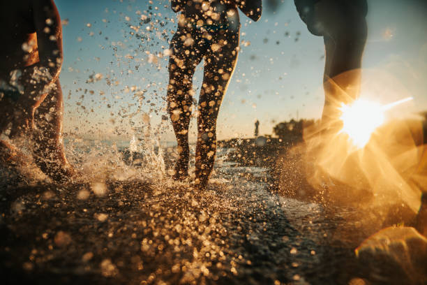 Brothers and sister having fun at sea, running on beach on sunny summer day, smiling and splashing