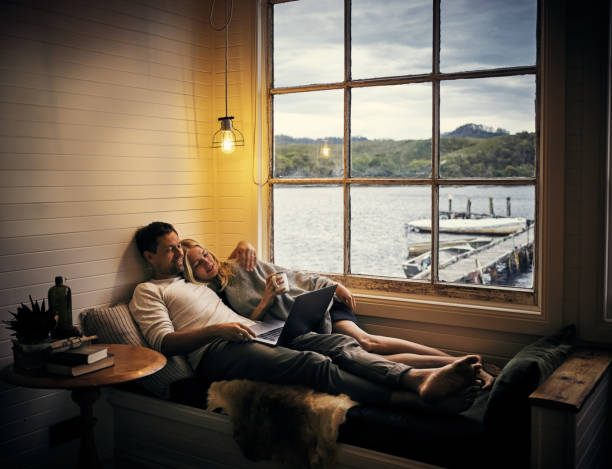 Accommodation that inspires relaxation Shot of a young couple using a laptop together while relaxing in their holiday home cottage life stock pictures, royalty-free photos & images