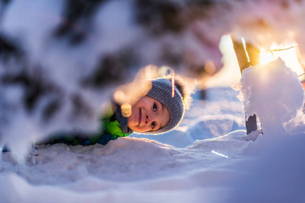 Winter portrait of a beautiful little boy having a lot of fun in snow. It’s sunset on the top of the mountain.