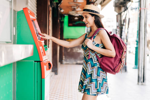 Young brunette girl traveler withdrawing money from ATM in Thailand, Asia. Young brunette girl traveler withdrawing money from ATM in Thailand, Asia. 20s Hispanic female backpacker in summer dress doing financial lifestyle. atm photos stock pictures, royalty-free photos & images