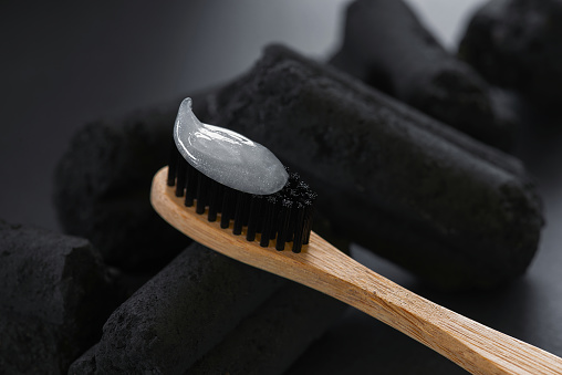 Bamboo toothbrush with charcoal bristles and toothpaste on the charcoal pieces, closeup