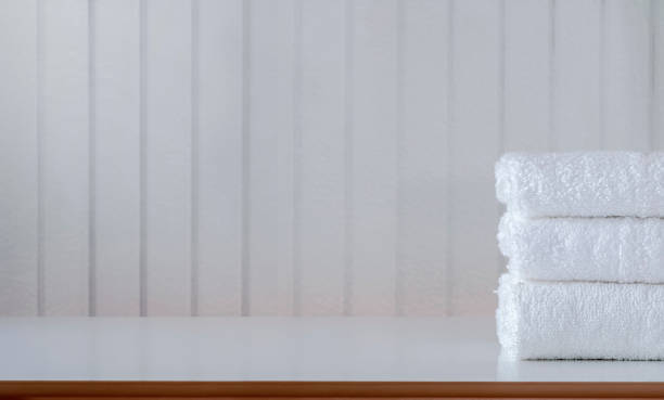 istock Stack of folded white towels on white top table with white wooden wall, copy space. 1254764522