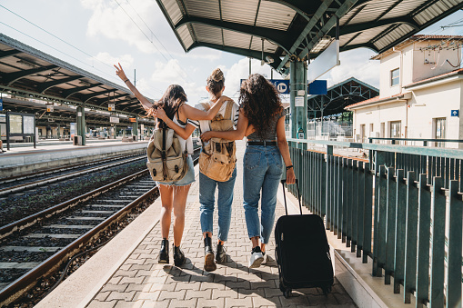 Three friends enjoying a trip together - Rear view. They are at a railroad train station.