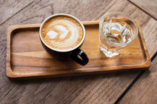 Cup of cappuccino and glass of water on wooden try and table