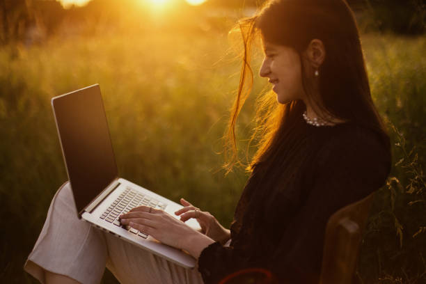 freelance and remote work outdoors. young business woman working online. fashionable elegant girl with laptop sitting on rustic chair in sunny summer field at sunset. creative image - child office chaos computer monitor imagens e fotografias de stock