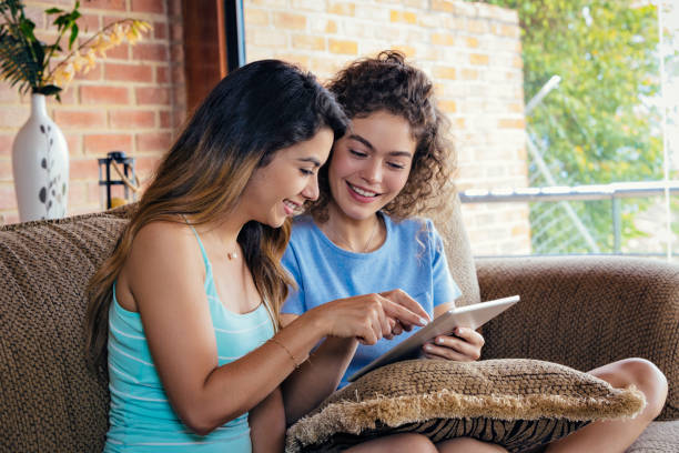 istock Hispanic young women friends surfing the net using digital tablet while relaxing on a sofa 1254768771