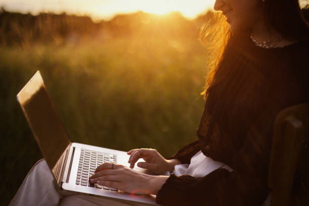 freelance and remote work outdoors. fashionable elegant girl with hands on keyboard sitting in sunny summer field at sunset.young business woman working online on laptop. creative image - child office chaos computer monitor imagens e fotografias de stock