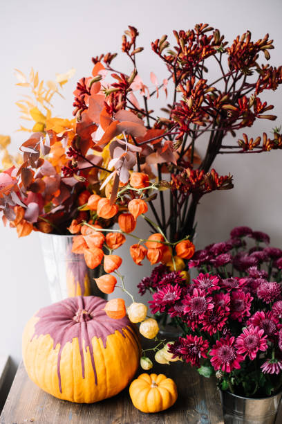 Fall inspired still life: pumpkin painted purple, pink chrysanthemum and other flowers in orange and red colors on the rustic wooden table stock photo