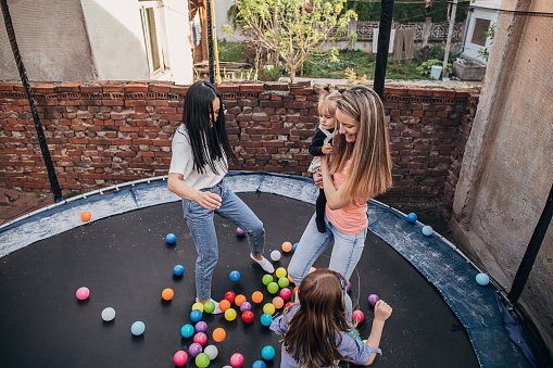 Four people, young mothers playing with their daughters together in trampoline