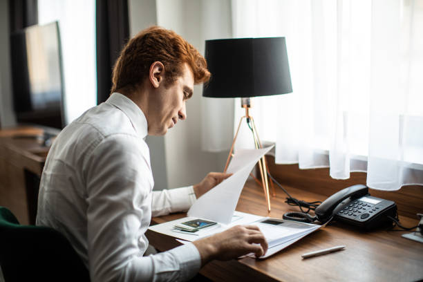 istock Businessman sitting at desk at hotel suite and looking at document 1254775918