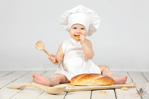 Child cook. Little girl in cook clothes with a big bun and flour. The girl is one year old. A child with an Easter bun. Funny kid in a culinary hat.