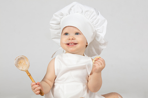 Child cook. Beautiful little girl in cook clothes with a big spoon. The child is one year old. Funny baby is laughing. Little chef. The concept of cooking food.