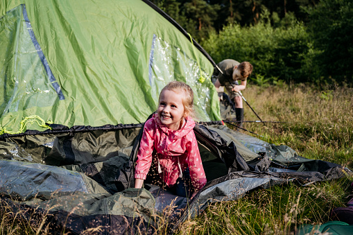 Active 5 year old blonde girl smiling as she helps her brother set up tent for overnight camping in late spring.