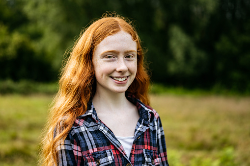 Partial front view of longhaired 15 year old Caucasian girl wearing casual clothing and smiling at camera with greenery of natural parkland in background.
