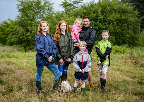 Full length front view of mid adult parents with children aged 5-15 and dog smiling at camera in natural parkland.