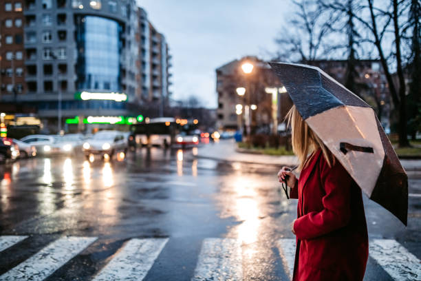 woman crossing street downtown in rain - rainy weather imagens e fotografias de stock