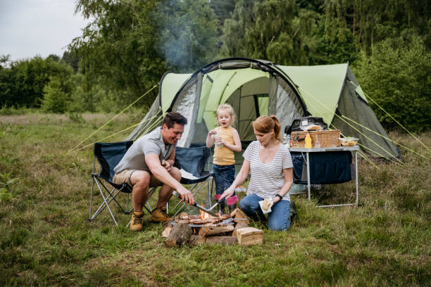 famiglia con un bambino che cucina a fuoco aperto durante il campeggio - campeggiare foto e immagini stock