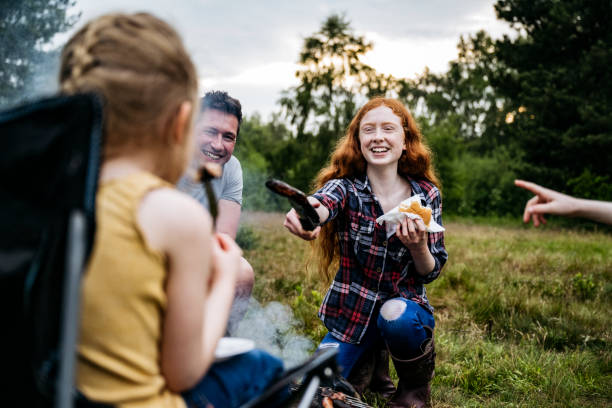 adolescente que ofrece joven hermana quemada salchicha en la cocina - camping family vacations eating fotografías e imágenes de stock