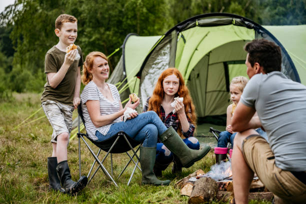 Relaxed family enjoying cookout on weekend camping trip Caucasian family with three children aged 5-15 smiling as they eat meal grilled over open fire while camping in woodland area. nottinghamshire stock pictures, royalty-free photos & images