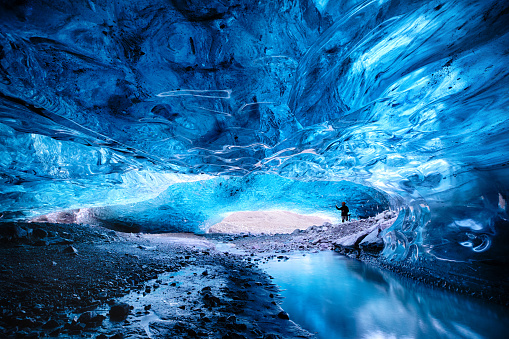 Inside a blue glacial ice cave in the glacier. Breioarmerkurjokull, part of the Vatnajokull glacier in southeast Iceland. A man is taking a photo and serves to demonstrate the scale.