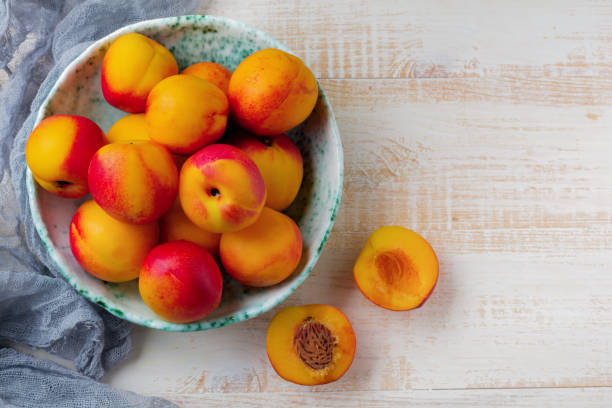 istock Fresh juicy fruit nectarines in ceramic bowl  on  white wooden background. Selective focus. Top view. Rustic style. 1254779517