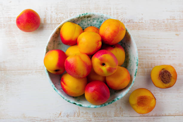 istock Fresh juicy fruit nectarines in ceramic bowl  on  white wooden background. Selective focus. Top view. Rustic style. 1254779668