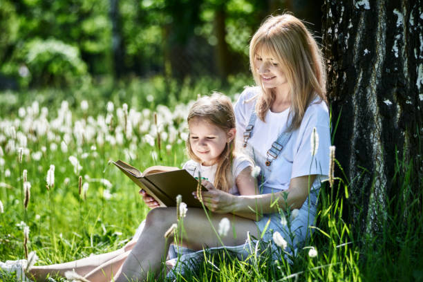 istock Mother and daughter sitting on grass reading a book 1254784358