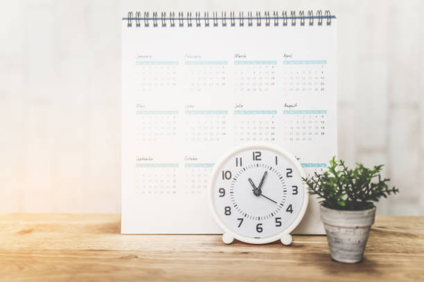 istock white analog clock with blurred white calendar and plant on wooden desk 1254787857