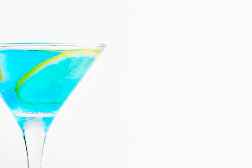 Cool blue cocktail in a glass with ice and a slice of lemon. Refreshing summer alcoholic and non-alcoholic drinks. Copy space