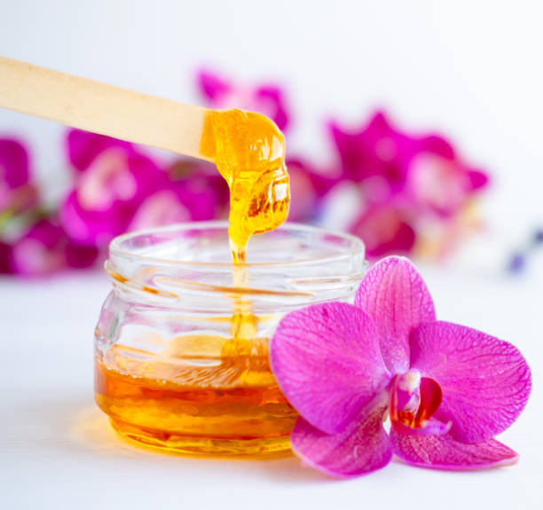istock sugar paste or wax honey for hair removing flows down from wooden waxing spatula sticks. flower background - depilation and beauty concept 1254788224