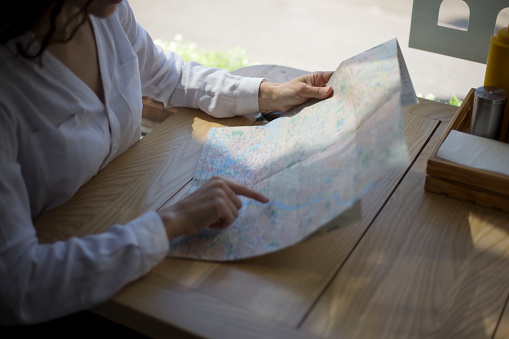 Horizontal view. Closeup image of women's hand pointing on a map, seated at the table in cafe.