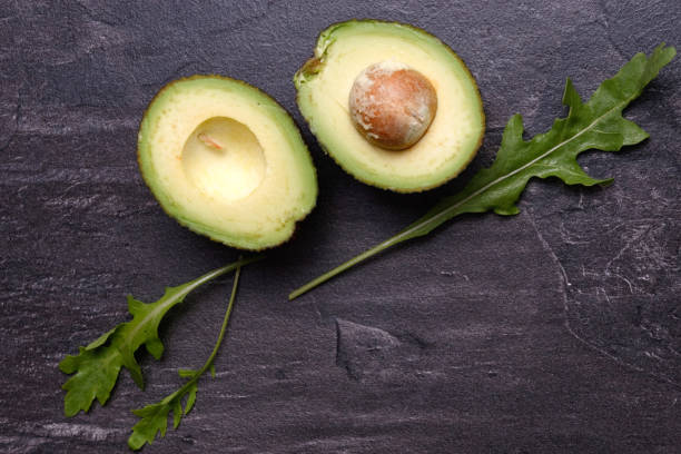 istock Two halves of avocado, one with a bone on a dark background. 1254795928