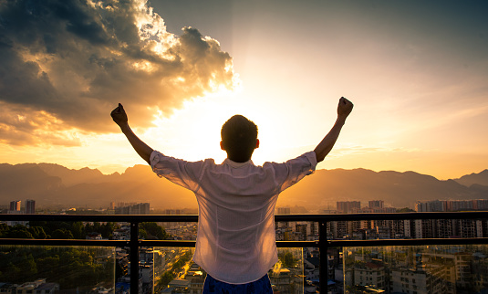 Young man standing on rooftop with arm raised