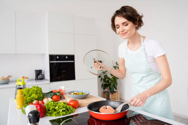 foto de linda dona de casa alegre senhora colocar filé de salmão fresco cru grande bife na panela voadora desfrutar bom cheiro mantendo dieta cozinhando jantar saudável usar avental cozinha moderna dentro de casa - prepared fish - fotografias e filmes do acervo