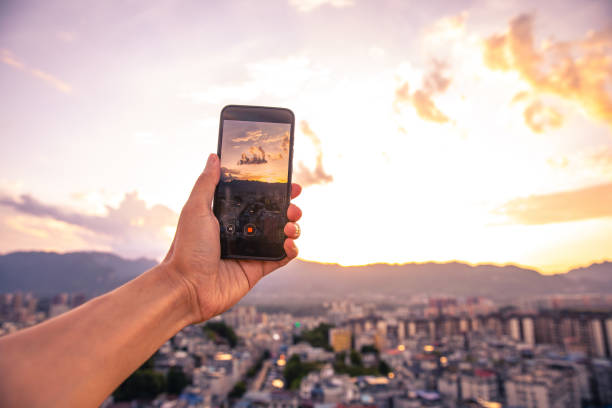 istock Hand holding mobile phone recording city sunset 1254796551