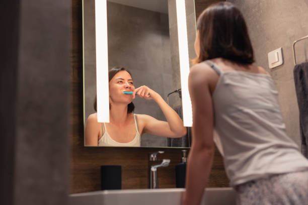 istock Woman brushing teeth next to bathroom sink 1254797791